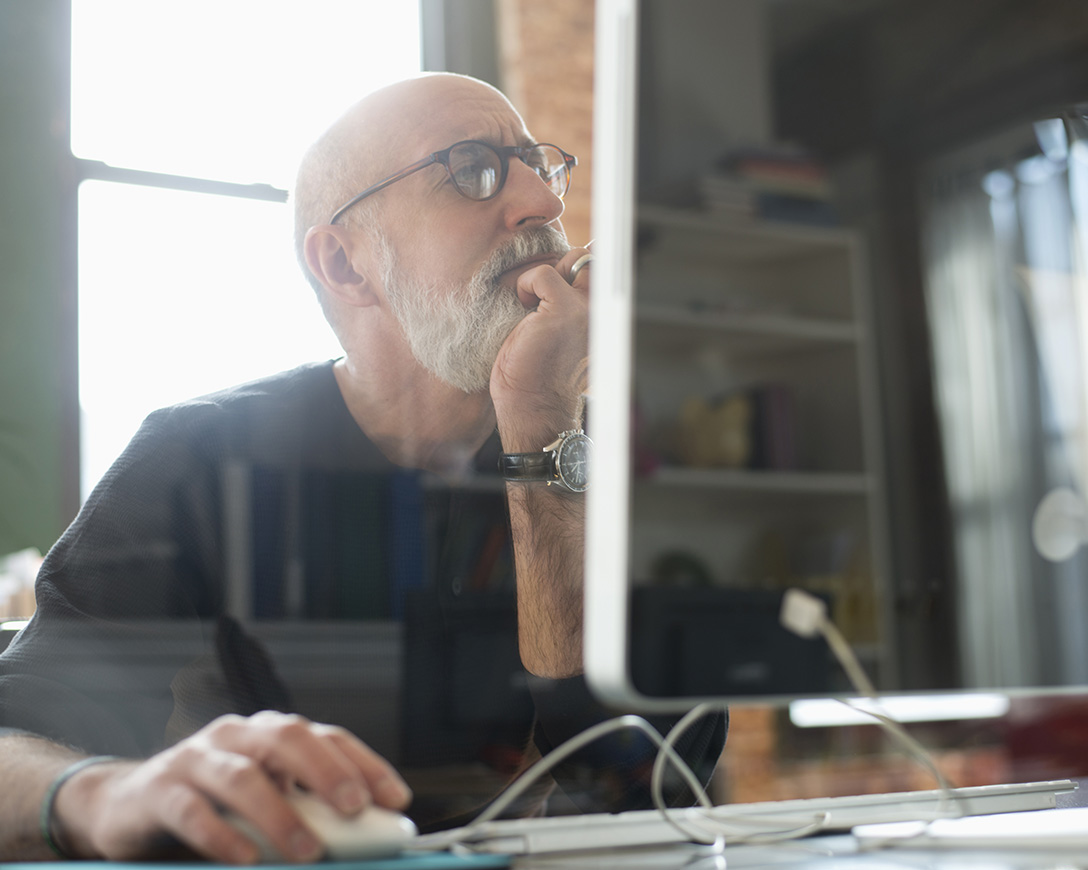 Cyber Resilience &ndash; A man rests his chin in his hand and gazes thoughtfully at his desktop monitor