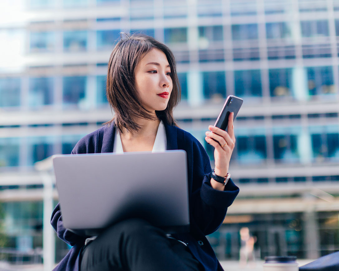 Optimization &ndash; A businesswoman working on a laptop and smartphone outside in the financial district